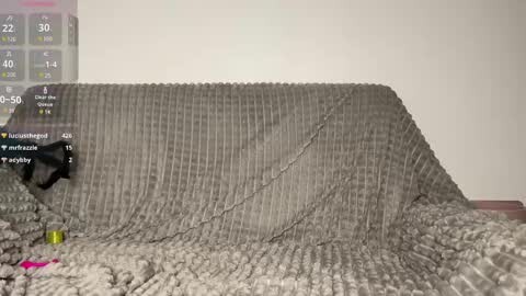 Media: Video of a beige, textured, ribbed blanket with a black ribbon tied at the center. The background shows a plain, light-colored wall with a digital clock displaying 20:32.