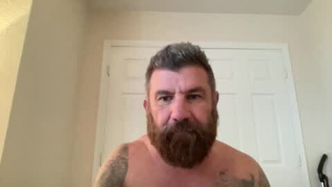Media: Video of a shirtless, bearded white man with a muscular build, tattoos on his arms, and a serious expression. He stands in front of a white door in a beige room.