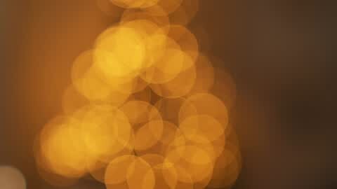 Media: A video of soft, glowing, golden-yellow bokeh circles against a dark brown background, creating a warm, ethereal ambiance with a subtle, abstract, and dreamy effect.