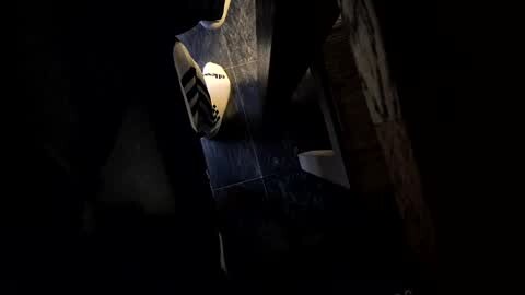 Media: A dimly lit video of a man's foot in a white sock, partially obscured by a dark, textured background. The man is wearing a dark, patterned shirt.