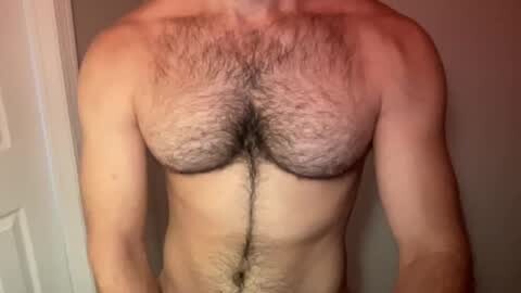 Media: Video of a shirtless man with light skin, displaying a hairy chest and abdomen. He stands in front of a plain, light-colored door. The image focuses on his torso, with a neutral background.