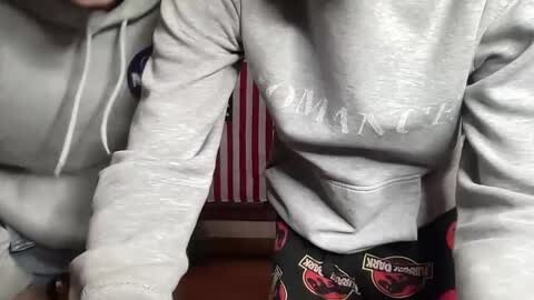 Media: A video showing a person wearing a grey sweatshirt with \"WELCOME\" in white letters and black shorts with red and white graphics. The background features a red and white striped pattern.