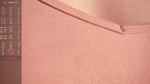 Media: Video of a close-up, textured, ribbed pink fabric with a soft, pastel background. A small, dark, rectangular label with white text is visible on the left.