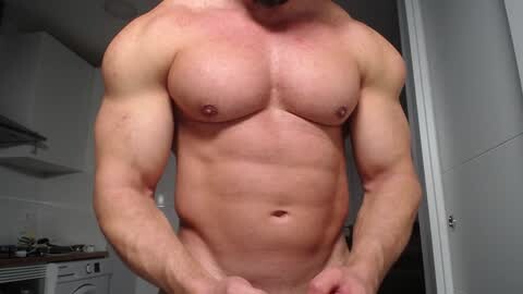 Media: Video of a muscular, shirtless man with fair skin, showing his six-pack abs and defined chest, standing in a modern kitchen with white cabinets and appliances.