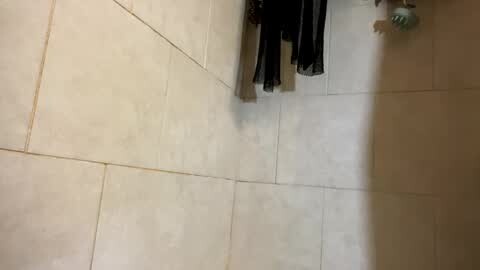 Media: Video of a beige-tiled bathroom floor with a shadowy figure wearing black pants and a white shirt, standing near the sink. The image is slightly out of focus.