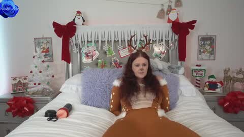 Media: Video of a woman in a reindeer costume on a bed, surrounded by festive decorations, including Christmas lights, ornaments, and a blue rose.