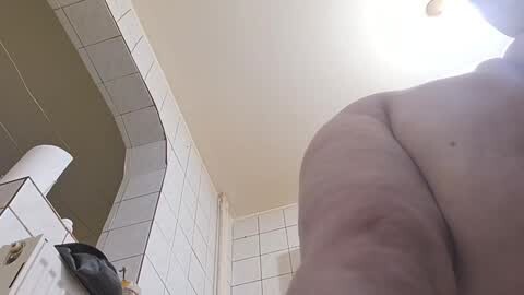 Media: Video of a close-up of a naked person's buttocks in a tiled bathroom with a white ceiling, beige walls, and a white sink.