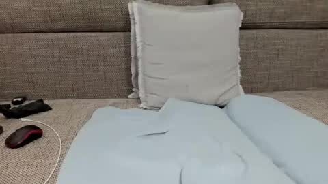 Media: Video of a beige couch with a light blue pillow and duvet, featuring a white corded phone and a pair of black headphones on the left side.