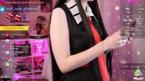 Media: Video of a light-skinned woman with black hair, wearing a black sleeveless top and red tie, holding a controller, in a room with pink and purple decor, with a chatbox overlay.