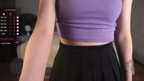 Media: Video of a light-skinned woman wearing a tight, ribbed, purple crop top and a high-waisted black pleated skirt, standing indoors with a virtual reality headset on, displaying a digital menu on the left.