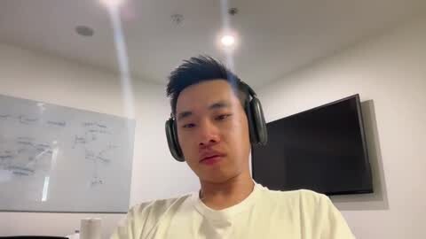 Media: Video of an Asian man in a studio wearing headphones, white t-shirt, in a room with white walls, a whiteboard, and a flat-screen TV.